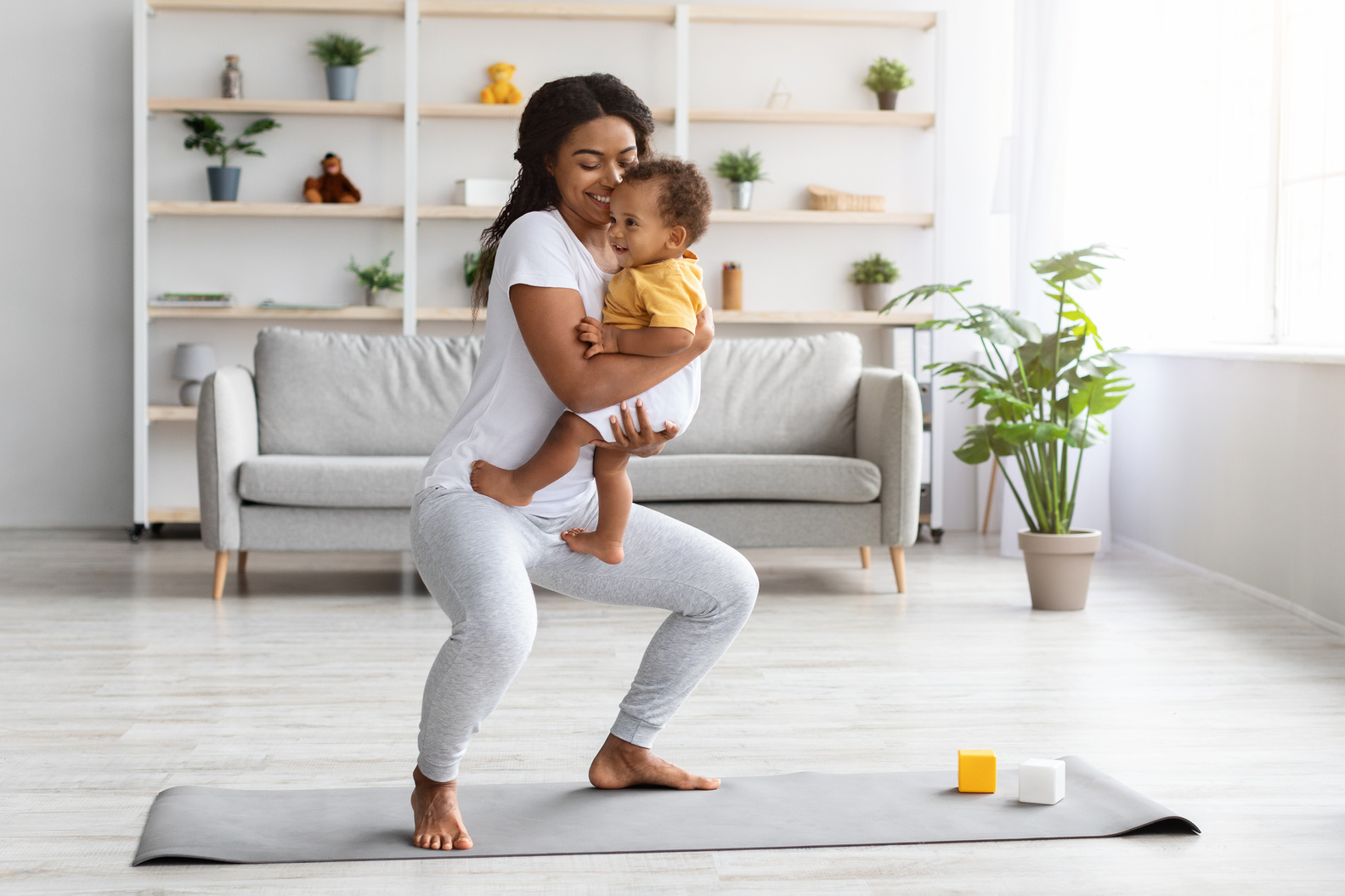Postpartum Weight Loss. Happy Black Lady Making Squats With Baby On Hands